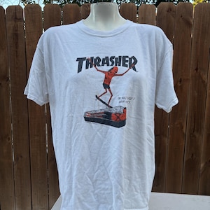 Pu&ograve; includere: T-shirt bianca con il logo Thrasher in rosso e nero. La grafica raffigura una figura di skateboard e il testo "OH YOU SEE? WHO SAYS". La maglietta &egrave; esposta su un manichino.