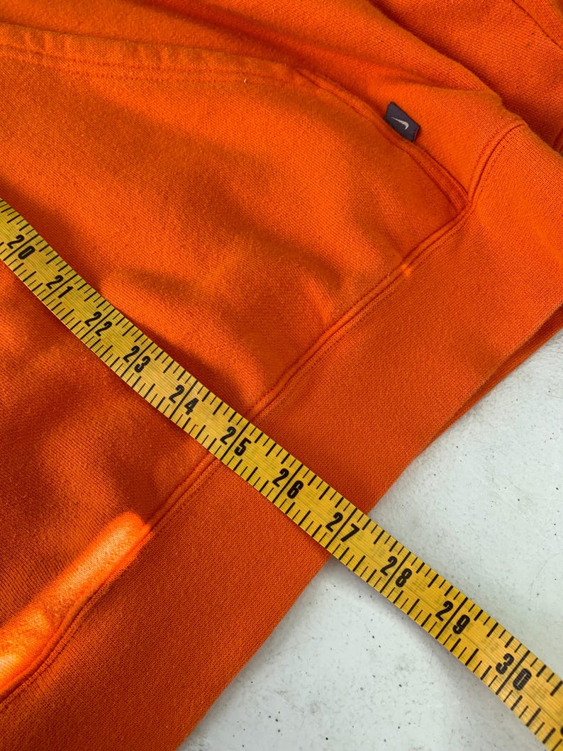 Peut inclure: Un sweat &agrave; capuche orange vif avec un petit logo bleu marine sur le haut de la poitrine gauche. Un m&egrave;tre ruban jaune est pos&eacute; sur le sweat &agrave; capuche, indiquant des mesures de 50,8 &agrave; 76,2 cm.
