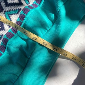 Puede incluir: Primer plano de una manga de sudadera turquesa con un estampado geom&eacute;trico en blanco, turquesa y morado. Una cinta m&eacute;trica amarilla se coloca sobre la manga, mostrando una medida de aproximadamente 56 cm.