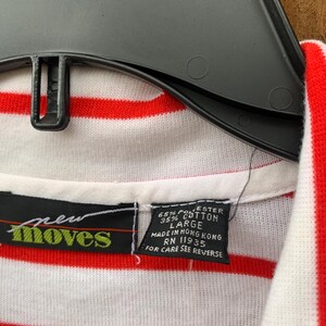 May include: A white and red striped shirt with a green "new moves" logo and a tag that reads "65% Polyester 35% Cotton Large Made in Hong Kong RN 11935 For Care See Reverse"