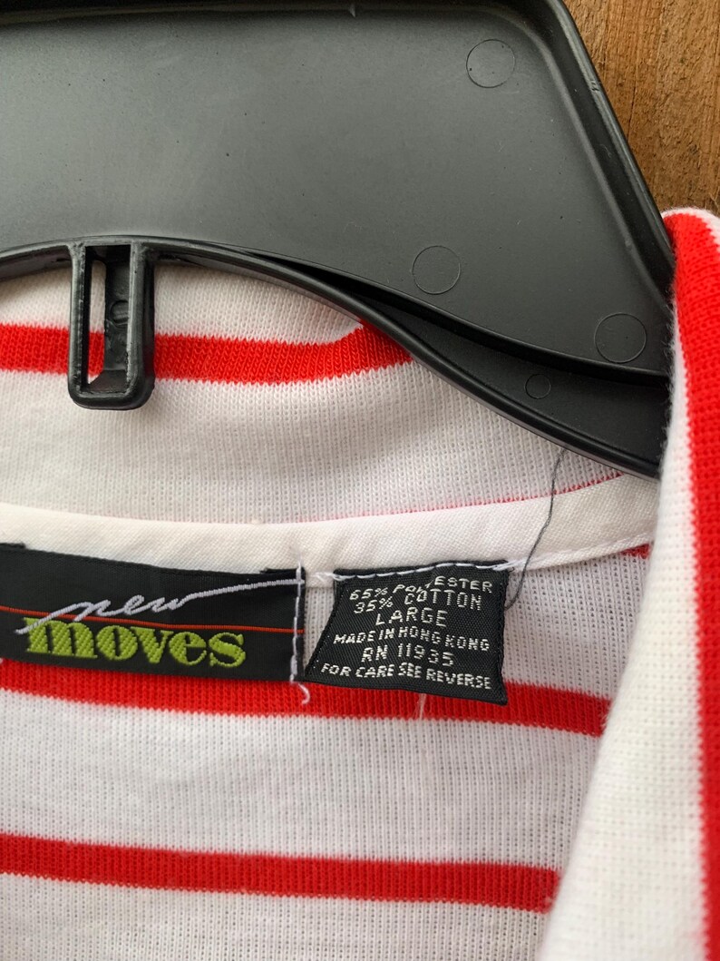 May include: A white and red striped shirt with a green "new moves" logo and a tag that reads "65% Polyester 35% Cotton Large Made in Hong Kong RN 11935 For Care See Reverse"