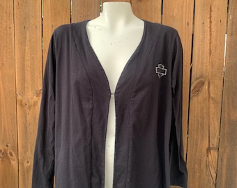 May include: Black long-sleeved cardigan with a deep V-neck and a small embroidered logo on the left side. The cardigan has a slit in the back.