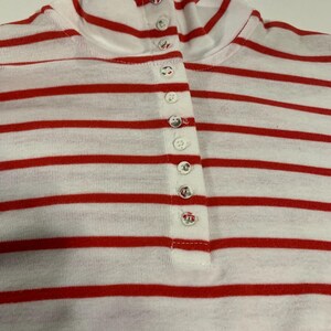 May include: A white and red striped long-sleeve shirt with a mock neck and a row of white buttons down the front.