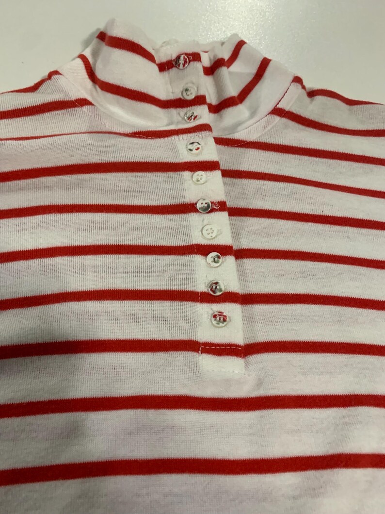 May include: A white and red striped long-sleeve shirt with a mock neck and a row of white buttons down the front.