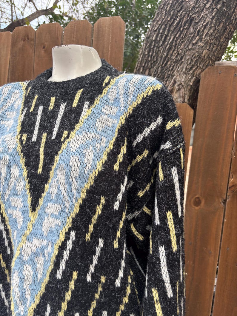 Puede incluir: Un su&eacute;ter gris con un patr&oacute;n geom&eacute;trico. El dise&ntilde;o incluye detalles en azul claro, amarillo y blanco. El su&eacute;ter tiene cuello redondo y mangas largas, perfecto para climas m&aacute;s frescos.