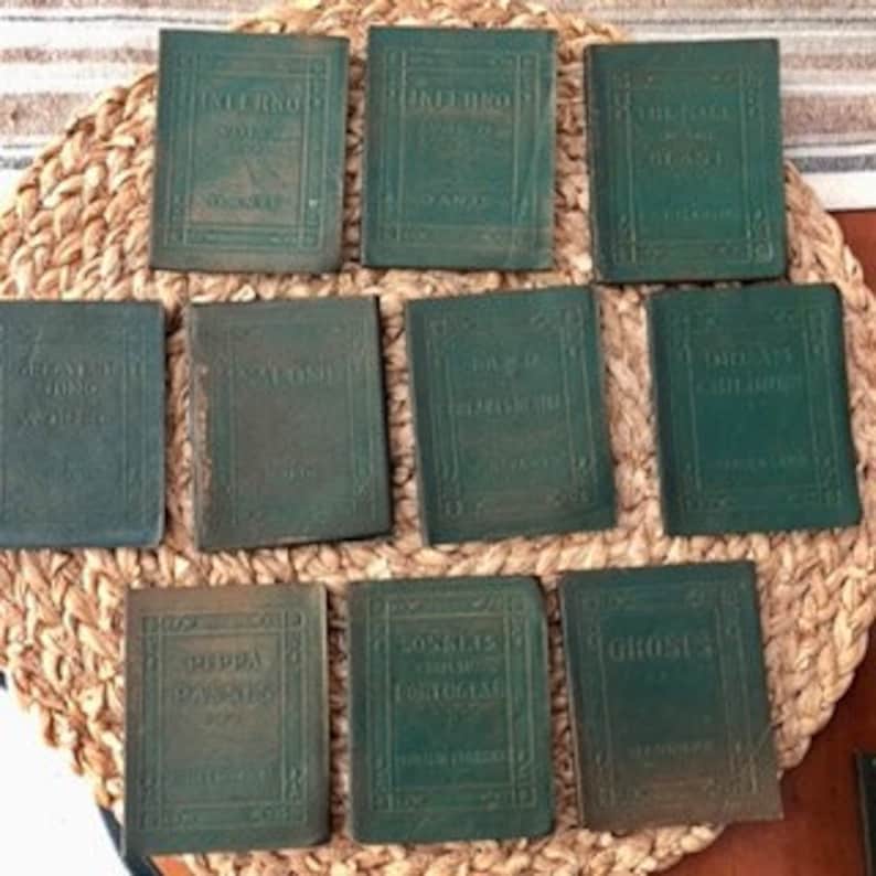 May include: Set of ten small, green, leather-bound books with gold lettering on the spines. The books are arranged in two rows of five. The titles on the spines include "The Iliad", "The Odyssey", "The Aeneid", "Don Quixote", "The Canterbury Tales", "The Decameron", "The Divine Comedy", "The Faerie Queen", "Hamlet", and "The Picture of Dorian Gray."