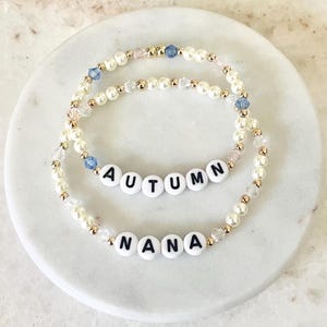 May include: Two beaded bracelets with gold accents. One bracelet spells "AUTUMN" and the other spells "NANA".