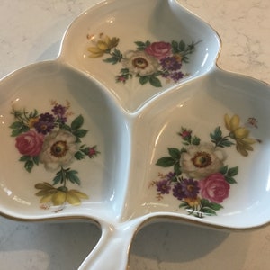 Puede incluir: Un plato de servir de cerámica blanca con forma de hoja con tres secciones. Cada sección tiene un diseño floral con flores rosas, blancas y amarillas.