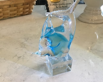 May include: A glass sculpture of a blue and clear fish on a clear glass base.