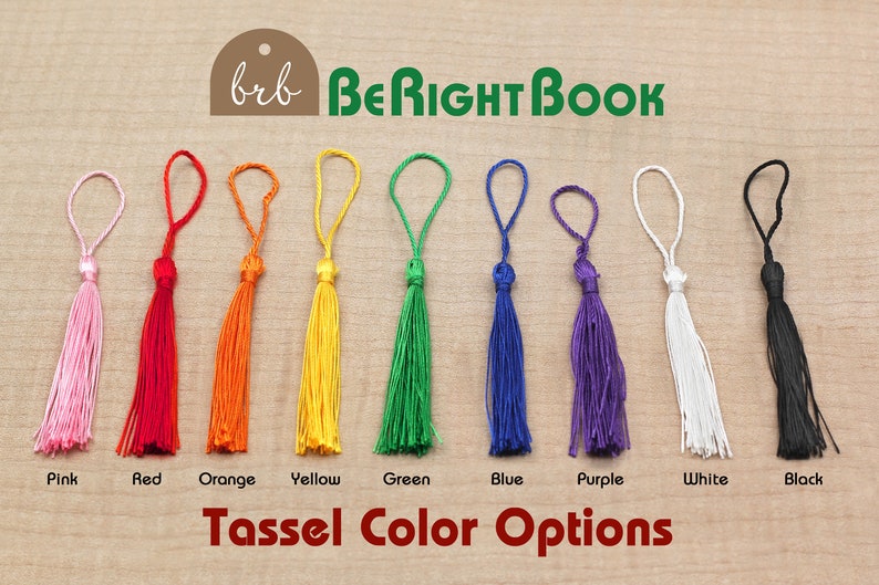 May include: A row of ten tassels in different colors, including pink, red, orange, yellow, green, blue, purple, white, and black. The tassels are arranged in a line on a wooden surface. The text "brb BeRightBook" and "Tassel Color Options" is visible below the tassels.