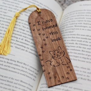 May include: Wooden bookmark with a cat illustration and the text "I have pawsed this book". The bookmark has a yellow tassel.