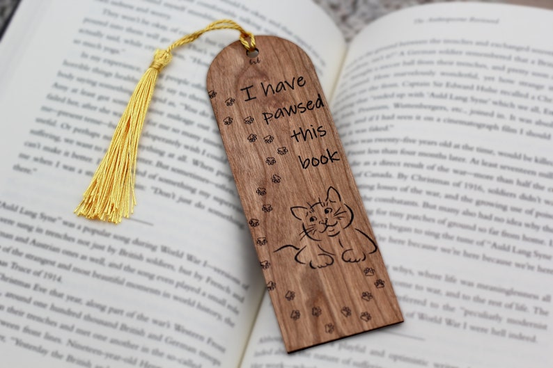 May include: Wooden bookmark with a cat illustration and the text "I have pawsed this book". The bookmark has a yellow tassel.