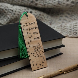 May include: Wooden bookmark with a green tassel, featuring a cat illustration and the text "I have pawsed this book".