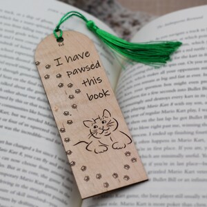 May include: A wooden bookmark with a green tassel. The bookmark features a cat illustration and the text "I have pawsed this book".