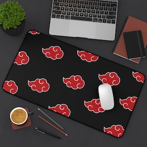 May include: Black rectangular desk mat featuring a repeating pattern of red clouds with white outlines. A white computer mouse rests on the mat, alongside a laptop, coffee cup, and stationery.