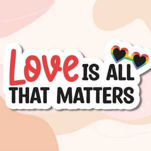 May include: A white sticker with the text "Love is all that matters" in black and red lettering. A rainbow heart-shaped sunglasses graphic is above the text.
