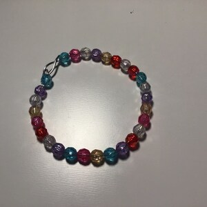 May include: A colorful beaded bracelet with a silver clasp. The beads are in shades of red, pink, purple, blue, yellow, and white.