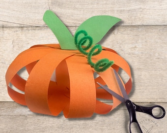 May include: A paper pumpkin craft with orange and green paper, a green pipe cleaner stem, and a pair of scissors.