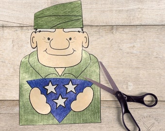 May include: A paper craft of a cartoon soldier holding a blue triangle with three white stars. The soldier is wearing a green hat and a green shirt. A pair of scissors is on the right side of the image.