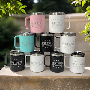 Puede incluir: Una colecci&oacute;n de nueve tazas de acero inoxidable con tapa, dispuestas en pir&aacute;mide. Cada taza presenta el texto 'FIRST FREE COFFEE BAR' rodeado por un c&iacute;rculo de puntos. Las tazas tienen acabados mate en colores rosa, blanco, turquesa y negro.