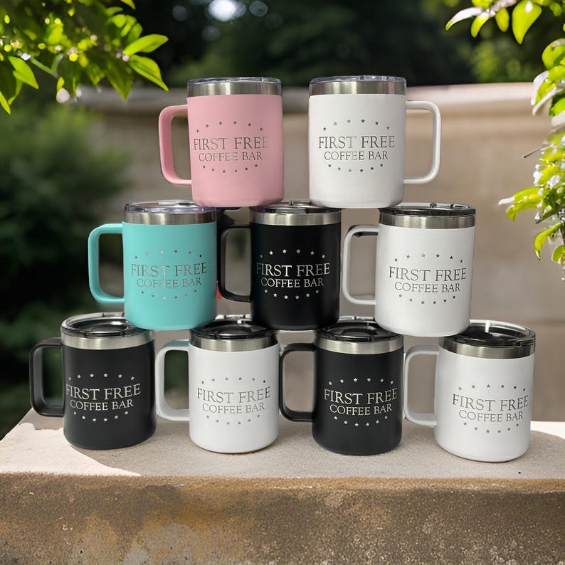Puede incluir: Una colecci&oacute;n de nueve tazas de acero inoxidable con tapa, dispuestas en pir&aacute;mide. Cada taza presenta el texto 'FIRST FREE COFFEE BAR' rodeado por un c&iacute;rculo de puntos. Las tazas tienen acabados mate en colores rosa, blanco, turquesa y negro.
