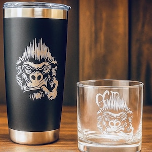 May include: A matte black stainless steel tumbler with a silver rim and a laser-engraved gorilla graphic, paired with a clear glass tumbler featuring the same etched gorilla design. Both containers display a detailed illustration of a gorilla face.