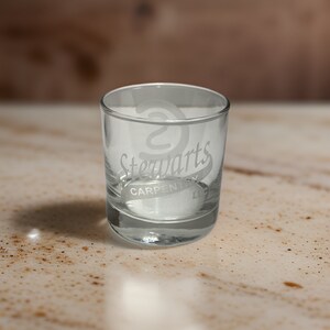 May include: A clear glass tumbler featuring an etched logo on the front. The design includes a stylized letter S above the text Stewarts, with the word CARPENTRY and the abbreviation LLC printed in a horizontal band underneath the main name.