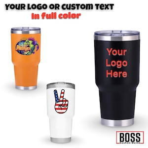 May include: Three stainless steel tumblers with different designs. The first tumbler is orange with a colorful graphic of a fish. The second tumbler is white with a peace sign graphic with the American flag colors. The third tumbler is black with the text "Your Logo Here" in red.