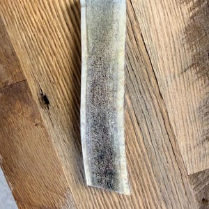 May include: A white ceramic mug with a black handle and the text "But First, Coffee" in a bold, black font. The mug is filled with a dark liquid, likely coffee, and sits on a light-colored surface.