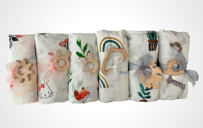 May include: Five white muslin swaddles with different colorful patterns, each tied with a ribbon and a wooden teether. The patterns include floral, rainbow, and animal prints.