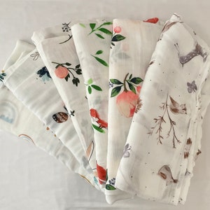 May include: A set of six white muslin swaddles with different woodland animal and floral prints. The swaddles are made of soft, breathable fabric and are perfect for keeping baby warm and cozy.