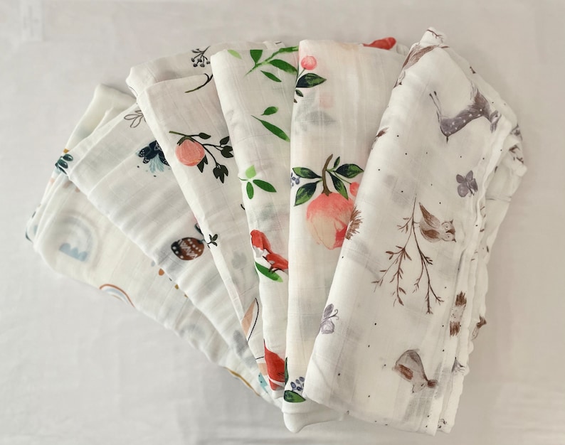 May include: A set of six white muslin swaddles with different woodland animal and floral prints. The swaddles are made of soft, breathable fabric and are perfect for keeping baby warm and cozy.