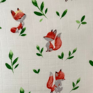 May include: White fabric with a repeating pattern of orange foxes and green leaves. The foxes are cartoon-like and have a simple design.