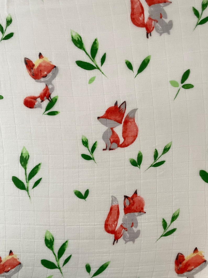 May include: White fabric with a repeating pattern of orange foxes and green leaves. The foxes are cartoon-like and have a simple design.