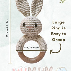 Pu&ograve; includere: Un sonaglio a forma di coniglio lavorato a uncinetto con un anello di legno. Il coniglio &egrave; beige e ha occhi neri e un naso rosa. L'anello ha un diametro di 7 cm. Il testo "Large Ring is Easy to Grasp" &egrave; scritto in nero su sfondo bianco.