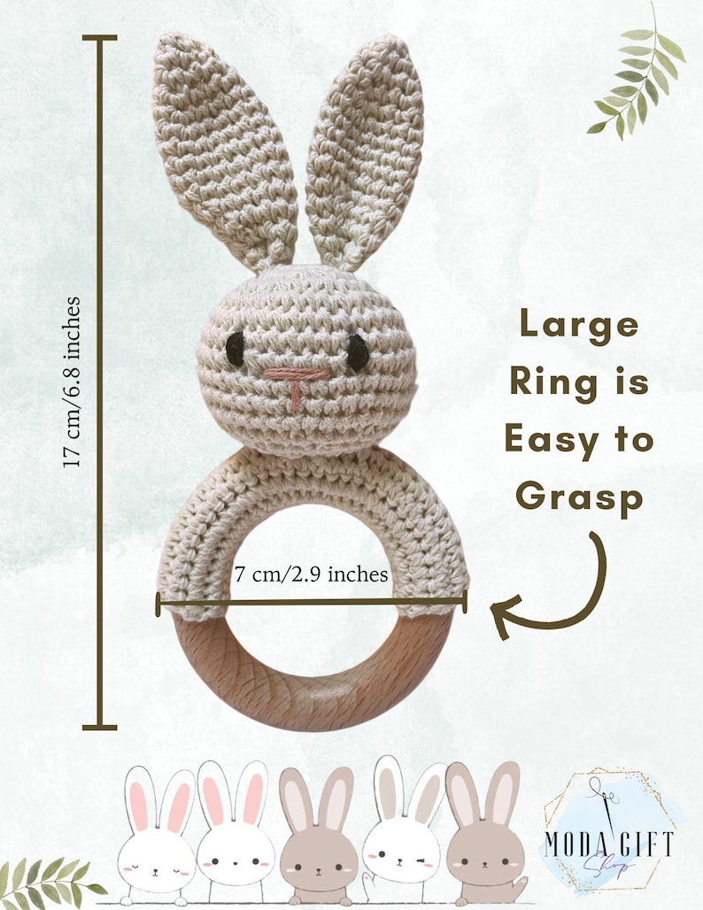 Pu&ograve; includere: Un sonaglio a forma di coniglio lavorato a uncinetto con un anello di legno. Il coniglio &egrave; beige e ha occhi neri e un naso rosa. L'anello ha un diametro di 7 cm. Il testo "Large Ring is Easy to Grasp" &egrave; scritto in nero su sfondo bianco.