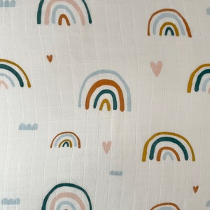 May include: White muslin fabric with a repeating pattern of colorful rainbows and hearts. The rainbows are in shades of blue, green, orange, and pink.