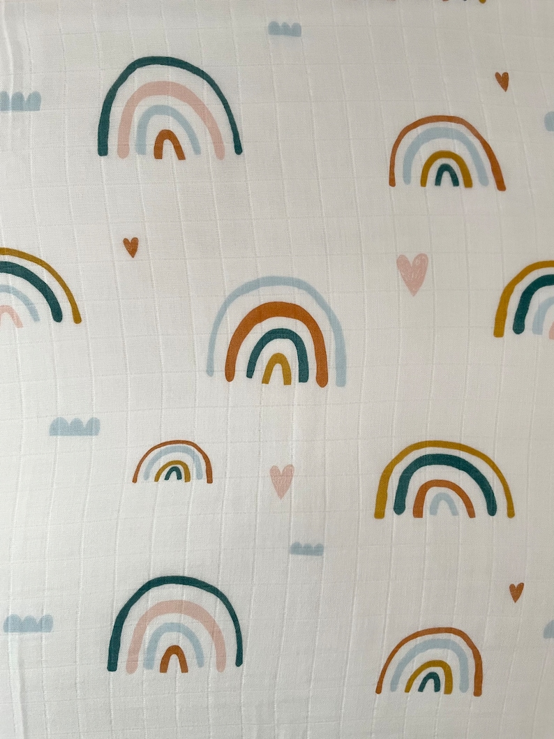 May include: White muslin fabric with a repeating pattern of colorful rainbows and hearts. The rainbows are in shades of blue, green, orange, and pink.