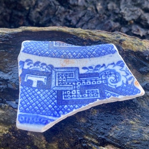 May include: A blue and white ceramic shard with a floral pattern. The shard is broken and has a rough edge.