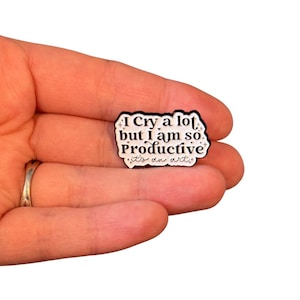 May include: White enamel pin with black text that reads "I cry a lot but I am so Productive it's an art."