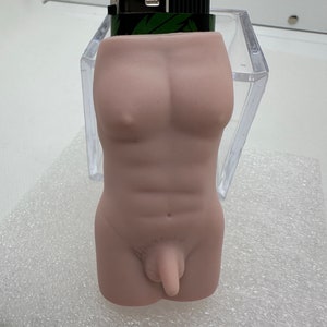 May include: A nude-colored lighter holder shaped like a human torso. The lighter holder is made of a smooth, matte material. The lighter holder is sitting on a white, textured surface.