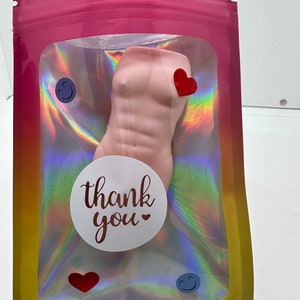 May include: A pink, sculpted torso with a thank you sticker and hearts in a clear plastic bag with a holographic iridescent background.