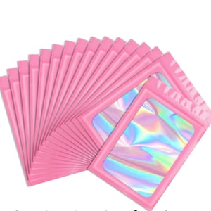 May include: A collection of pink, resealable pouches with a clear, iridescent window. The pouches are arranged in a fan shape, showcasing the holographic effect of the window material. The pink color is consistent across all pouches.