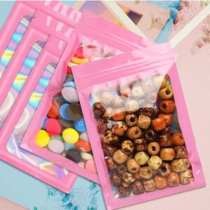 May include: Several pink, resealable bags with clear windows. One bag contains colorful candies, while others hold wooden beads in various shades of brown and tan. The bags have a holographic, iridescent strip on the side.