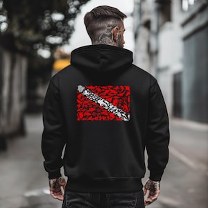 May include: Black hoodie with a red and white graphic design on the back. The design features a diagonal white and black element over a red background with a pattern of various shapes. The hoodie has a hood and long sleeves.