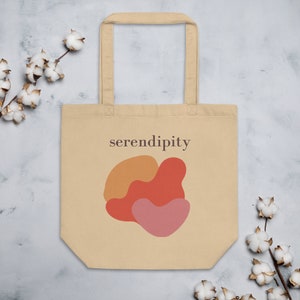 Puede incluir: Una bolsa de tela beige con un dise&ntilde;o de formas abstractas en naranja, rojo y rosa. La bolsa tiene un asa marr&oacute;n y el texto "serendipity" impreso en la parte delantera.