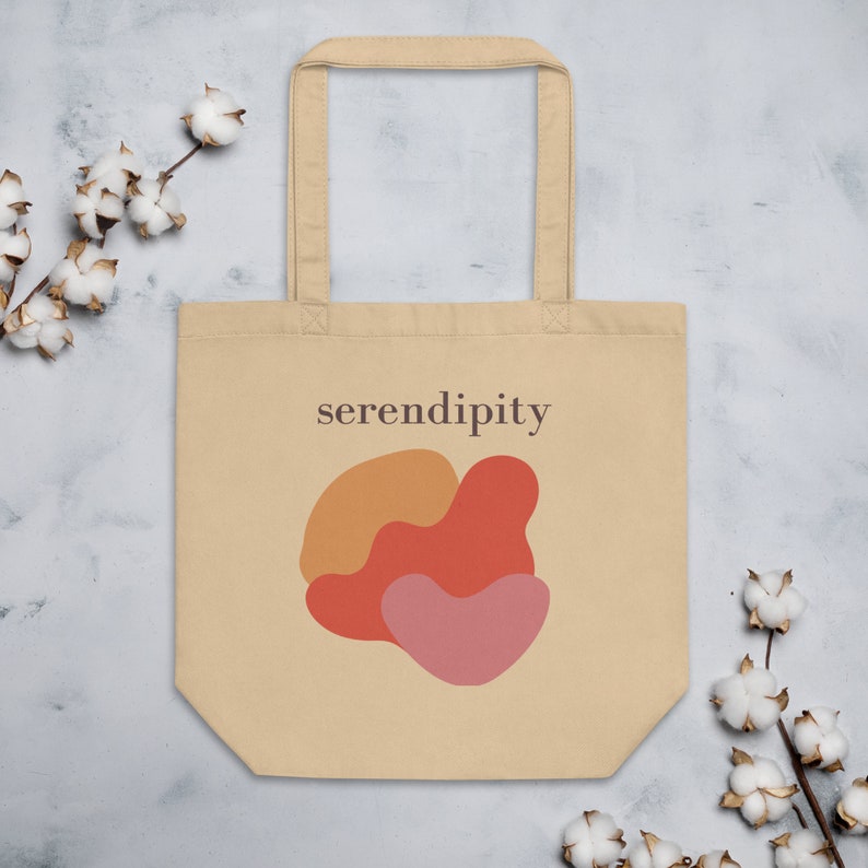 Puede incluir: Una bolsa de tela beige con un dise&ntilde;o de formas abstractas en naranja, rojo y rosa. La bolsa tiene un asa marr&oacute;n y el texto "serendipity" impreso en la parte delantera.