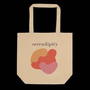 Puede incluir: Una bolsa de tela beige con un dise&ntilde;o gr&aacute;fico de tres formas abstractas en naranja, rojo y rosa. El texto "serendipity" est&aacute; impreso en marr&oacute;n en la bolsa.