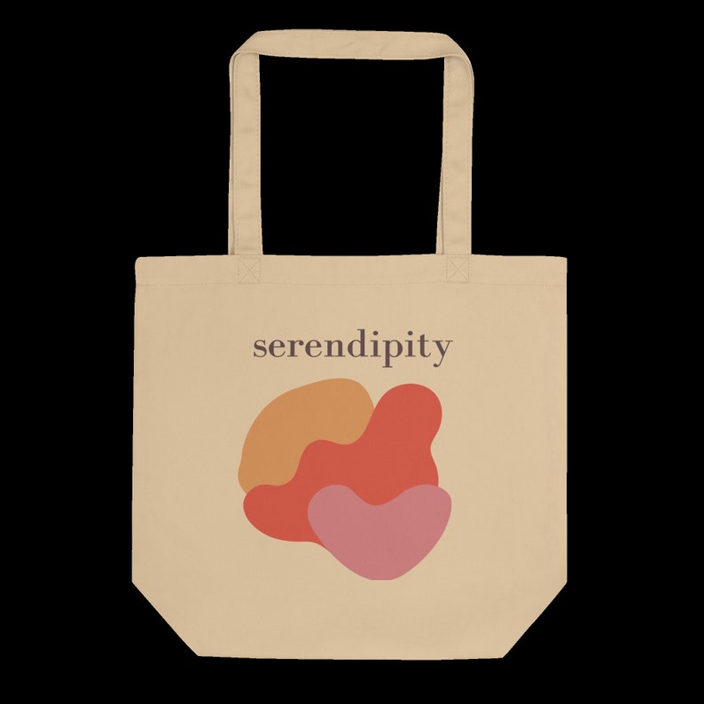 Puede incluir: Una bolsa de tela beige con un dise&ntilde;o gr&aacute;fico de tres formas abstractas en naranja, rojo y rosa. El texto "serendipity" est&aacute; impreso en marr&oacute;n en la bolsa.