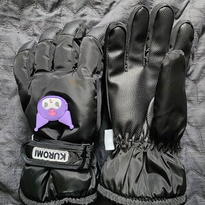 K&ouml;nnte beinhalten: Ein Paar schwarze Winterhandschuhe mit einer lilafarbenen Comicfigur auf einem Handschuh. Die Handschuhe haben einen schwarzen Riemen mit dem Wort "KUROMI" darauf.